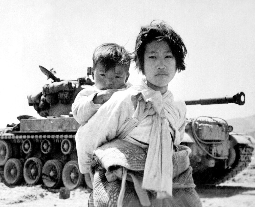 Korean war refugees walk past a tank