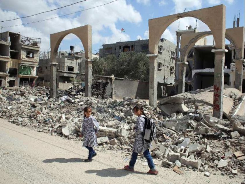 Palestinian girls walk past the rubble of a destroyed building.