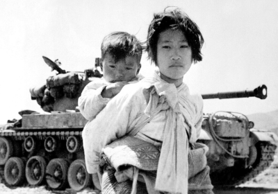 Korean war refugees walk past a tank