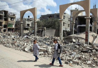 Palestinian girls walk past the rubble of a destroyed building.